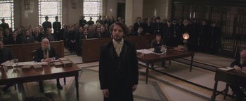 Movie still from “The Current War: Director's Cut” (2017), directed by Alfonso Gomez-Rejon – A man standing in front of a group of people in a court room; Medium shot, Over the shoulder angle