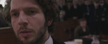 Movie still from “The Current War: Director's Cut” (2017), directed by Alfonso Gomez-Rejon – A man's face in front of a group of people; Close Up shot, Over the shoulder angle
