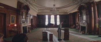 Movie still from “The Current War: Director's Cut” (2017), directed by Alfonso Gomez-Rejon – A man standing in a large room with a piano; Wide shot, High angle