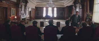 Movie still from “The Current War: Director's Cut” (2017), directed by Alfonso Gomez-Rejon – A group of people sitting around a piano in a room; Wide shot, Over the shoulder angle