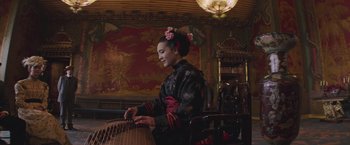 Movie still from “The Current War: Director's Cut” (2017), directed by Alfonso Gomez-Rejon – A woman in a black and red dress playing a guzheng; Medium shot, Low angle