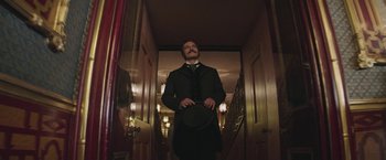 Movie still from “The Current War: Director's Cut” (2017), directed by Alfonso Gomez-Rejon – A man standing in a hallway holding a hat; Medium shot, Low angle