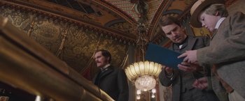 Movie still from “The Current War: Director's Cut” (2017), directed by Alfonso Gomez-Rejon – A man standing next to another man in front of a chandelier; Medium shot, Low angle