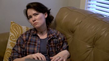 Movie still from “The Curse of Professor Zardonicus” (2022), directed by Gabriel Theis – A woman sitting in a chair with a book in her lap; Close Up shot, Over the shoulder angle