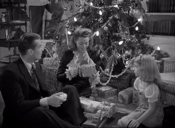 Movie still from “The Curse of the Cat People” (1944), directed by Robert Wise – An old photo of a woman and two children opening gifts under a christmas tree; Medium shot, High angle