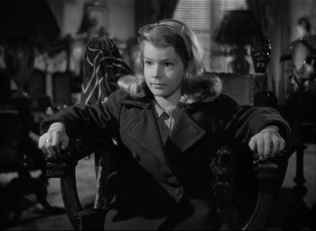 Movie still from “The Curse of the Cat People” (1944), directed by Robert Wise – A young girl sitting in a chair wearing a trench coat; Medium shot, High angle