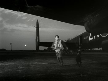 Movie still from “The Dam Busters” (1955), directed by Michael Anderson – A man walking on the ground next to an airplane; Wide shot, Low angle