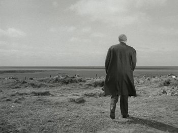 Movie still from “The Dam Busters” (1955), directed by Michael Anderson – An older man in a long coat is standing in a field; Wide shot, Low angle