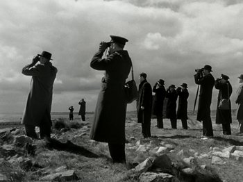Movie still from “The Dam Busters” (1955), directed by Michael Anderson – A black and white photo of a group of men standing on top of a rocky hill; Wide shot, Low angle