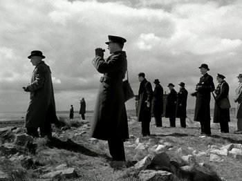 Movie still from “The Dam Busters” (1955), directed by Michael Anderson – A black and white photo of a group of men in a field; Wide shot, Low angle