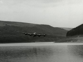 Movie still from “The Dam Busters” (1955), directed by Michael Anderson – An airplane is flying low over a body of water; Extreme Wide shot, Low angle