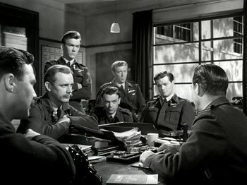 Movie still from “The Dam Busters” (1955), directed by Michael Anderson – A black and white photo of a group of men sitting around a table; Medium shot, High angle