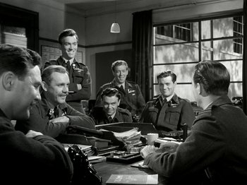 Movie still from “The Dam Busters” (1955), directed by Michael Anderson – A black and white photo of a group of men sitting around a table; Medium shot, High angle