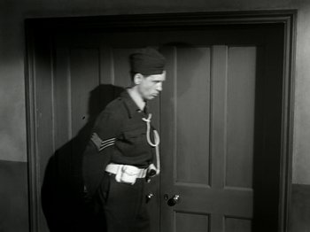 Movie still from “The Dam Busters” (1955), directed by Michael Anderson – A man in a uniform standing in front of a door; Medium shot, Low angle