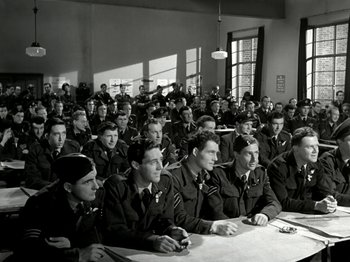 Movie still from “The Dam Busters” (1955), directed by Michael Anderson – A group of men sitting at a table in front of a window; Wide shot, High angle