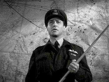 Movie still from “The Dam Busters” (1955), directed by Michael Anderson – A man in a uniform holding a stick in front of a map; Medium shot, Low angle