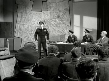 Movie still from “The Dam Busters” (1955), directed by Michael Anderson – A group of men sitting in front of each other in a room; Wide shot, High angle