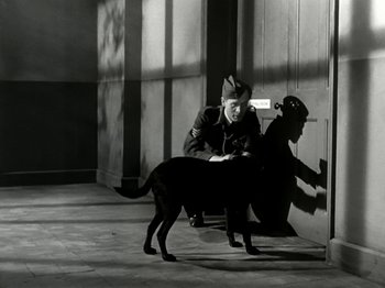 Movie still from “The Dam Busters” (1955), directed by Michael Anderson – A black and white photo of a man and a dog; Wide shot, High angle