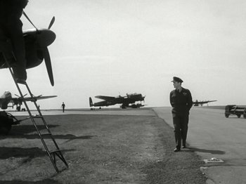 Movie still from “The Dam Busters” (1955), directed by Michael Anderson – An old black and white photo of an air force officer; Wide shot, Low angle