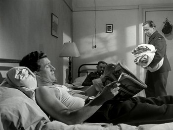 Movie still from “The Dam Busters” (1955), directed by Michael Anderson – A man reading a newspaper in bed while two other men watch; Medium shot, Over the shoulder angle