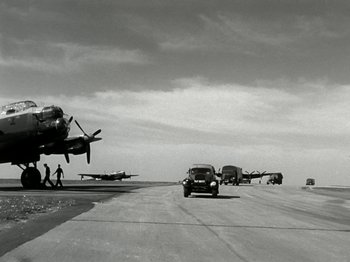 Movie still from “The Dam Busters” (1955), directed by Michael Anderson – An old photo of an airport with planes on the runway; Extreme Wide shot, Low angle