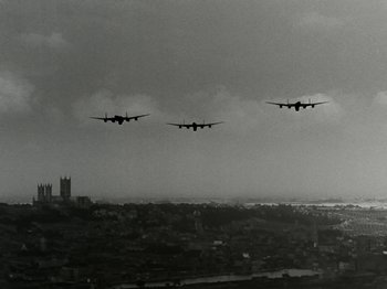 Movie still from “The Dam Busters” (1955), directed by Michael Anderson – Three airplanes flying in formation over a city; Extreme Wide shot, Low angle