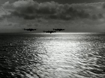 Movie still from “The Dam Busters” (1955), directed by Michael Anderson – A group of planes flying over a body of water under a cloudy sky; Extreme Wide shot, Low angle