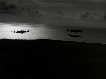 Movie still from “The Dam Busters” (1955), directed by Michael Anderson – Two planes flying over a body of water at dusk; Extreme Wide shot, High angle
