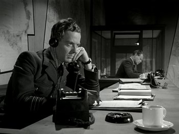 Movie still from “The Dam Busters” (1955), directed by Michael Anderson – Two men are sitting at a table with a phone; Medium shot, High angle