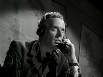 Movie still from “The Dam Busters” (1955), directed by Michael Anderson – A man talking on a phone while wearing headphones; Close Up shot, Low angle