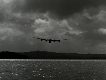 Movie still from “The Dam Busters” (1955), directed by Michael Anderson – An airplane is flying low over a body of water; Extreme Wide shot, Low angle