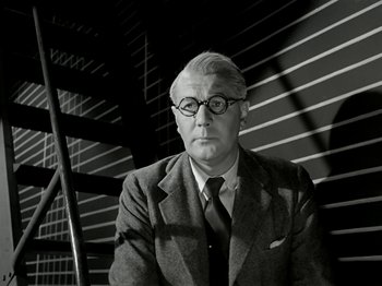 Movie still from “The Dam Busters” (1955), directed by Michael Anderson – An older man wearing glasses and a suit; Close Up shot, Low angle
