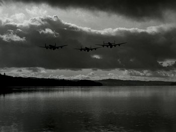 Movie still from “The Dam Busters” (1955), directed by Michael Anderson – Three planes flying in formation over a body of water under a cloudy sky; Extreme Wide shot, Low angle
