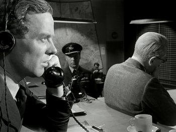 Movie still from “The Dam Busters” (1955), directed by Michael Anderson – An old photo of a man on the phone with another man in the background; Medium shot, Over the shoulder angle