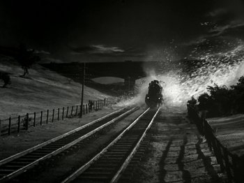 Movie still from “The Dam Busters” (1955), directed by Michael Anderson – A train traveling down train tracks at night time; Extreme Wide shot, High angle