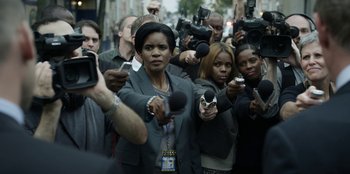 Movie still from “House of Cards” (2013), created by Beau Willimon – A group of people holding microphones in front of a crowd; Medium shot, High angle