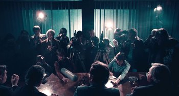 Movie still from “The Damned United” (2009), directed by Tom Hooper – A group of people sitting around a table with microphones; Wide shot, High angle