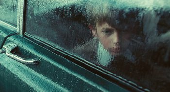 Movie still from “The Damned United” (2009), directed by Tom Hooper – A boy looking out of a car window through a rain covered window; Close Up shot, Low angle