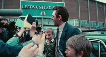 Movie still from “The Damned United” (2009), directed by Tom Hooper – A man in a suit and tie standing in front of a crowd; Wide shot, Over the shoulder angle