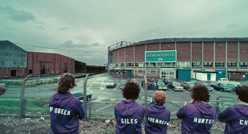 Movie still from “The Damned United” (2009), directed by Tom Hooper – A group of young men standing next to each other in front of a stadium; Wide shot, High angle