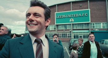 Movie still from “The Damned United” (2009), directed by Tom Hooper – A group of people taking pictures in front of a building; Close Up shot, High angle