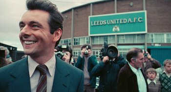 Movie still from “The Damned United” (2009), directed by Tom Hooper – A group of people taking pictures in front of a building; Close Up shot, Over the shoulder angle