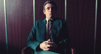 Movie still from “The Damned United” (2009), directed by Tom Hooper – A man sitting in a chair wearing a suit and tie; Medium shot, Low angle