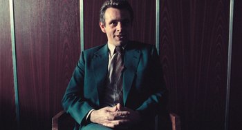 Movie still from “The Damned United” (2009), directed by Tom Hooper – A man sitting in a chair wearing a suit and tie; Medium shot, Low angle