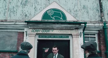 Movie still from “The Damned United” (2009), directed by Tom Hooper – A man standing in front of a building; Wide shot, High angle
