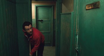 Movie still from “The Damned United” (2009), directed by Tom Hooper – A man in a red jacket leaning against a green door; Medium shot, High angle