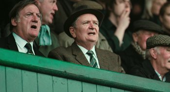 Movie still from “The Damned United” (2009), directed by Tom Hooper – An old man wearing a suit and a hat; Medium shot, Over the shoulder angle
