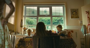Movie still from “The Damned United” (2009), directed by Tom Hooper – A woman sitting at a table with two children; Wide shot, Over the shoulder angle