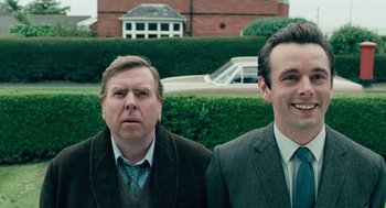 Movie still from “The Damned United” (2009), directed by Tom Hooper – Two men standing next to each other in front of a building; Medium shot, Over the shoulder angle