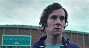 Movie still from “The Damned United” (2009), directed by Tom Hooper – A man with long brown hair looking to his left; Close Up shot, Over the shoulder angle